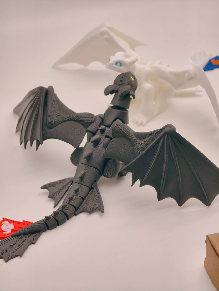 A black articulated dragon toy with spread wings, shown on a light gray surface with a white dragon figure blurred in the background.