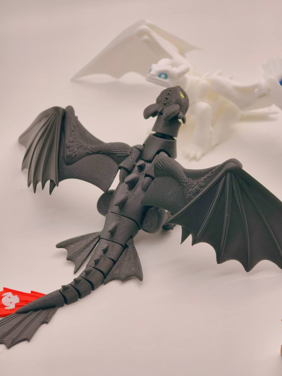 A black articulated dragon toy with spread wings, shown on a light gray surface with a white dragon figure blurred in the background.